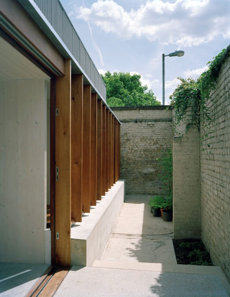 A photo of a wood and concrete house taken from its narrow garden.
