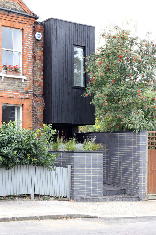 A photograph of an unusual black wooden building at the end of a terrace.
