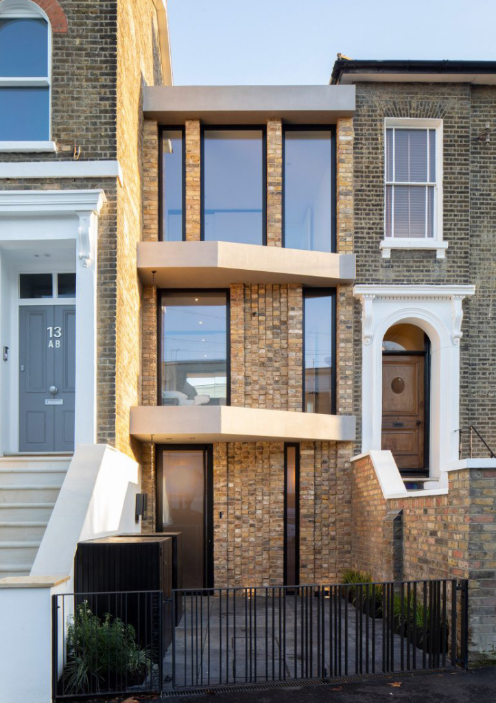 A photograph of a thin contemporary brick and concrete house, between two existing terraced houses of different heights.
